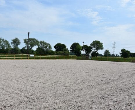View Looking into the large equestrian, equine riding arena, with sand & fibre surface surrounded by timber post & rail fence with telegraph poles and arena lighting showing. Located In North Yorkshire
